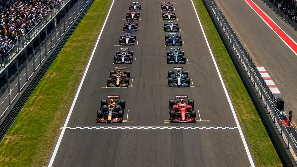 Largada de uma corrida de Fórmula 1 vista de cima, com os carros alinhados no grid