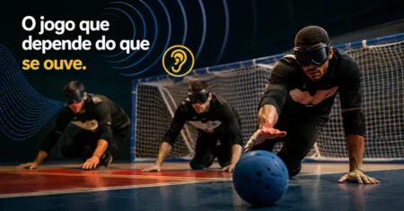 Três atletas de goalball vendados em posição de defesa no chão da quadra, com a bola de guizos rolando rente ao piso diante do gol