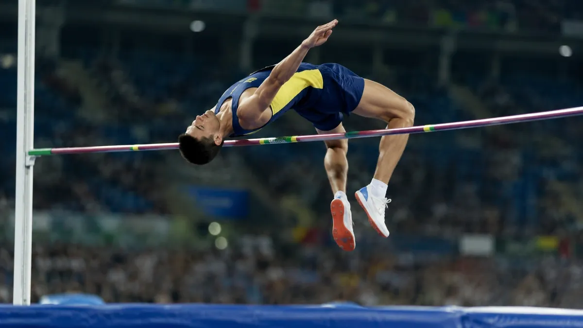 Atleta de salto em altura transpondo o sarrafo de costas com o corpo arqueado na técnica Fosbury Flop